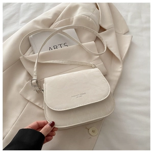 Détail du sac selle beige à texture plissée et bandoulière réglable sur fond neutre