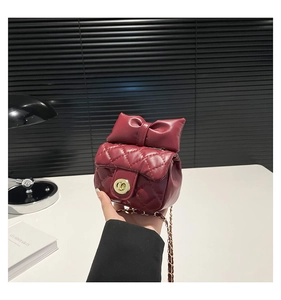 Close-up of wine red quilted chain bag with bow detail and gold twist lock clasp