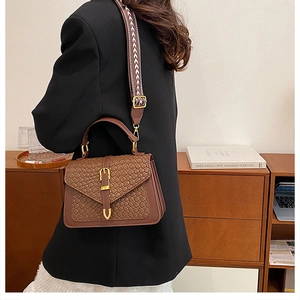 Macro shot of brown faux leather handbag with woven texture and gold metal buckle