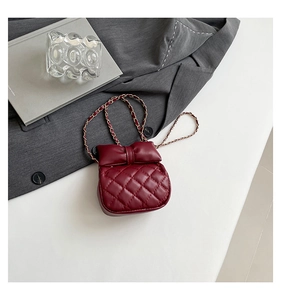Detail of burgundy quilted mini bag with bow flap and elegant gold chain strap