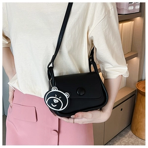 Close-up of black crossbody bag with round buckle and cute bear charm in cozy room