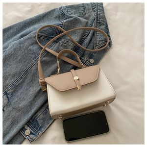 Détail du sac bandoulière bicolore élégant avec boucle dorée sur tissu blanc et jean