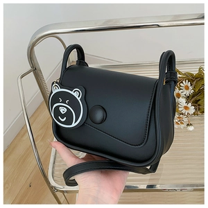 Detail of minimalist black leather crossbody bag with cute bear charm and carry handle