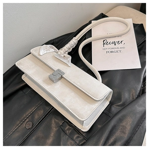 Close-up of a white rectangular handbag with a crystal buckle and silk scarf on the strap