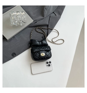 Close-up of quilted black crossbody bag with large bow and gold lock near a smartphone