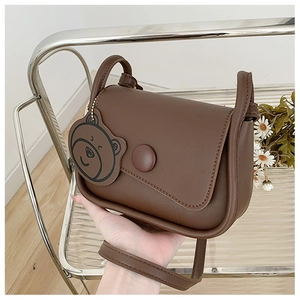 Close-up of brown mini crossbody bag with unique flap, round buckle and cute bear charm