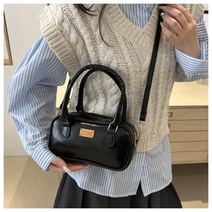 Detail of black bowling bag with gold hardware and removable strap held by a model