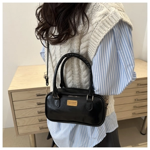 Detail of black faux leather Boston bag with gold logo plaque shown on a model