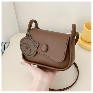 Close-up of brown PU leather shoulder bag featuring a cute cartoon bear pendant