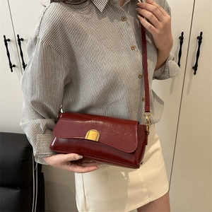 Fashionable dark red crossbody bag with golden clasp worn by a model in a minimalist setting