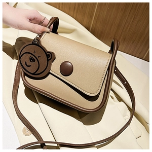 Detail view of khaki square shoulder bag with brown trim and cute bear keychain charm