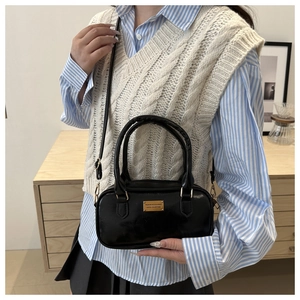Detail of black glossy bowling handbag with gold metal hardware on model in casual setting