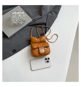 Mini brown quilted crossbody bag with bow detail and gold chain next to a phone