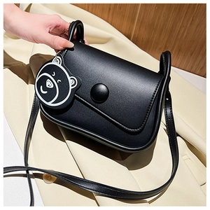 Detail of black mini flap bag featuring a large round clasp and cartoon bear charm