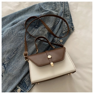 Détail du sac bandoulière vintage avec pieds dorés sur une veste en jean bleue