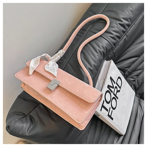Detail of pink shoulder bag featuring a silk scarf and rhinestone buckle on leather sofa