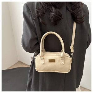 Detail of cream white leather bowling bag with gold metal plate on a grey blazer