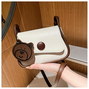 Close-up of cream square crossbody bag with brown trim and cute bear charm detail