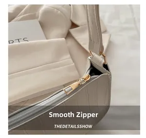 Detail of smooth golden zipper on cream crocodile pattern baguette shoulder bag