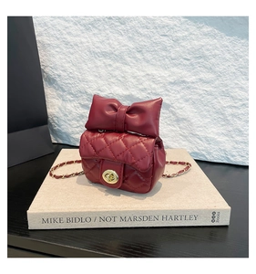 Macro view of burgundy quilted crossbody bag with a large bow and gold twist lock