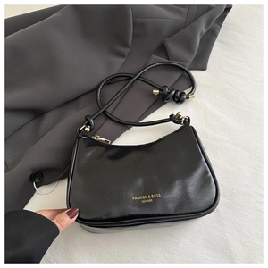 Detail of glossy black patent leather shoulder bag with gold zipper and brand lettering