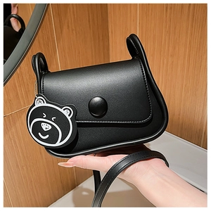 Detail of black faux leather crossbody bag with curved base and cute bear keychain