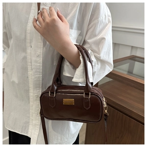 Detail of dark brown leather bowling bag with gold plaque and crossbody strap worn by model
