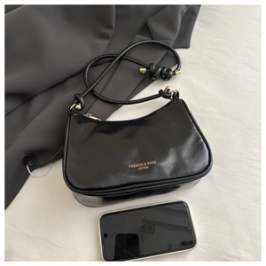 Close-up of matte black underarm bag with gold logo lettering and phone size reference