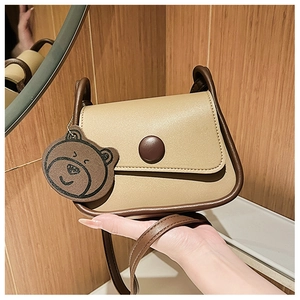 Close-up of beige and brown crossbody bag featuring a cute bear charm and round buckle
