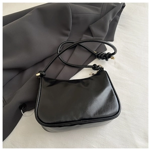 Detailed view of black faux leather underarm bag with gold zipper and knotted strap design