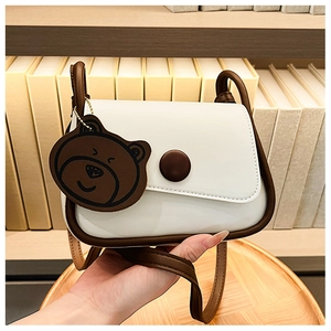 Detail of white and brown crossbody bag with round buckle and cute bear charm