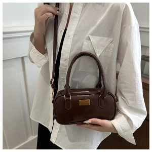 Detail of dark brown mini bowling bag with gold metal plaque and sleek handle
