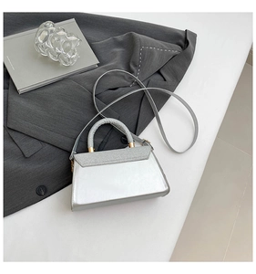 Close-up of silver crossbody bag with glitter texture and metallic handle on grey blazer