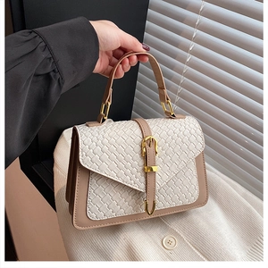 Detail of a beige woven texture flap and golden buckle on a brown leather crossbody bag