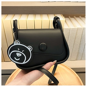Close-up of minimalist black square crossbody bag with round buckle and bear charm