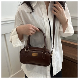 Detail of dark brown glossy leather bowling bag with gold plaque and crossbody strap
