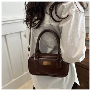 Detailed side view of vintage dark brown bowling handbag with gold metal logo plate