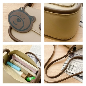 Detail view of beige square bag showing bear charm, interior space and shoulder strap