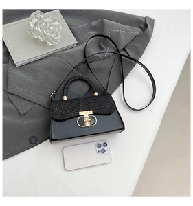 Detail of black crossbody bag with sequin handle, gold T-lock and smartphone for size