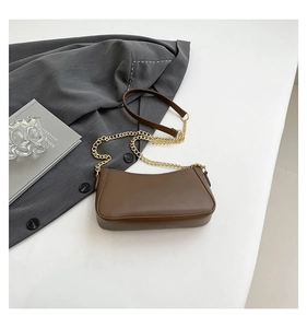 Detail of a brown leather underarm bag with gold chain strap on a white background