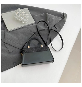 Detail of black crossbody bag featuring glitter handle and textured flap in studio setting