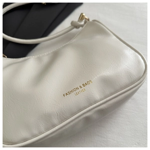 Detailed macro view of white crescent bag with gold lettering and polished hardware