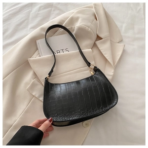 Detail of black crocodile texture baguette bag with golden zipper on beige suit
