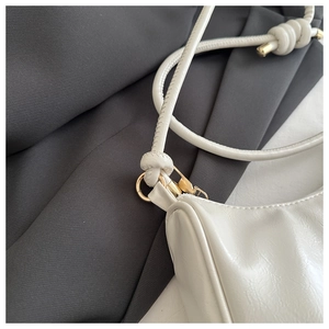 Detailed macro view of white patent leather shoulder bag with golden hardware and knots