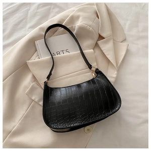 Detail of black faux crocodile leather crescent bag on a beige blazer background