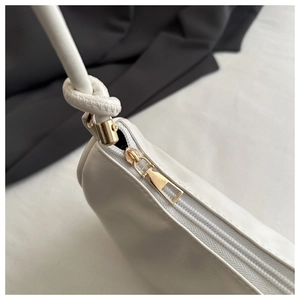 Detail of a white leather handbag featuring a gold zipper and knotted strap design