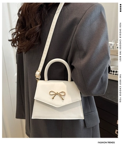 Detailed view of white leather handbag with golden bow hardware and a slim shoulder strap