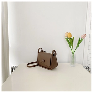 Detail of a dark brown PU leather crossbody bag featuring a round decorative buckle and soft curves