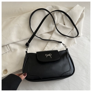 Detail of a black leather crossbody bag featuring a silver metal bow and flap closure