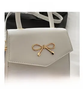 Detail of white leather mini handbag featuring a decorative gold bow clasp and stitching